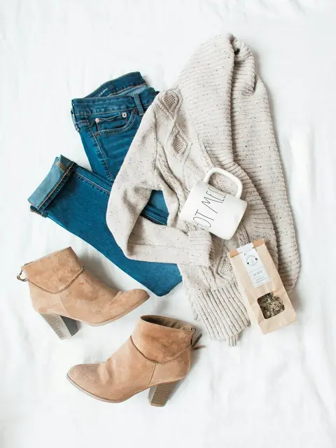 Flat lay of a cream long cardigan with blue jeans and tan ankle boots