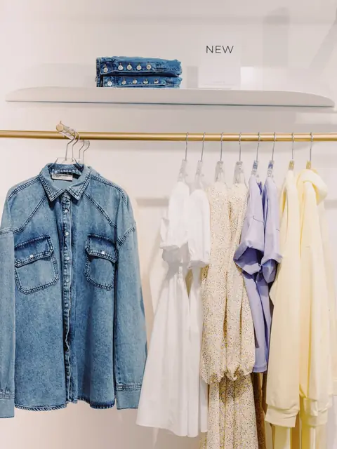 Denim shirt hanging on a brass rail beside white tops