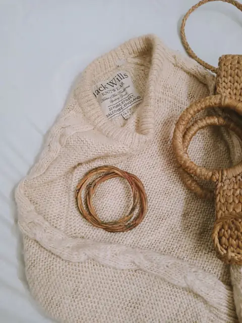 Oatmeal cable-knit sweater laid flat with woven bangles